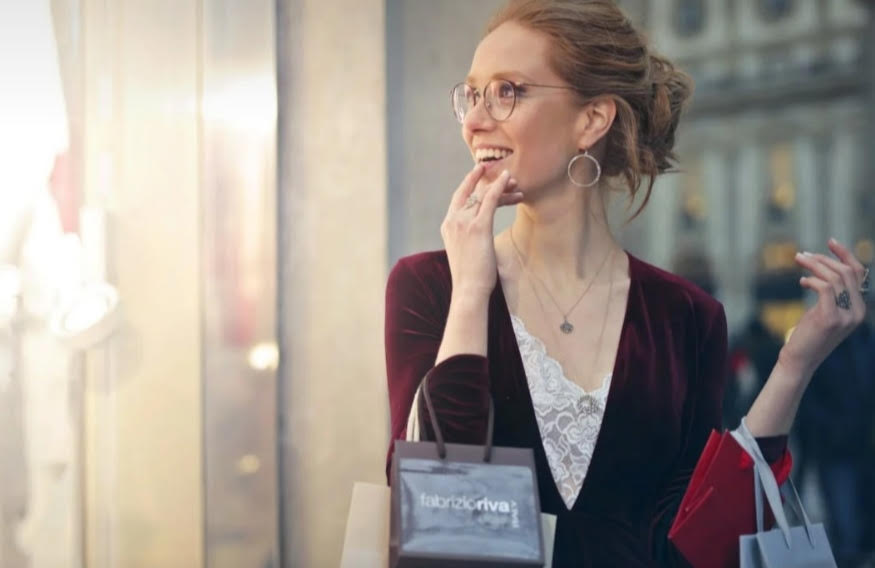 mujer rubia sonriendo con bolsas en la mano frente a escaparate de tienda